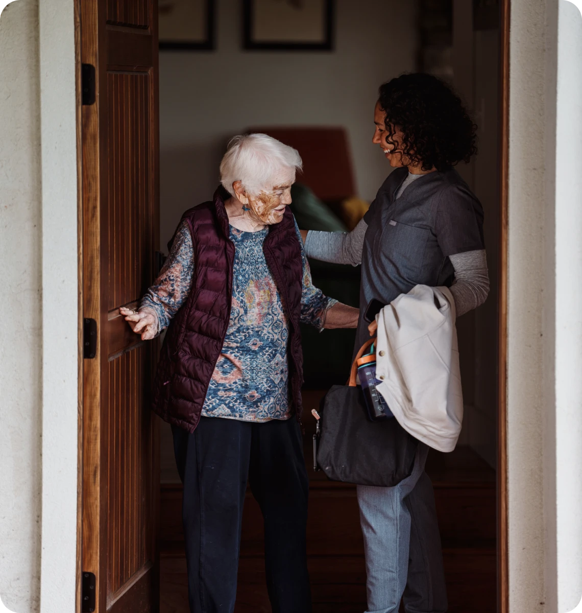 A young woman helping an elderly woman at the doorway.