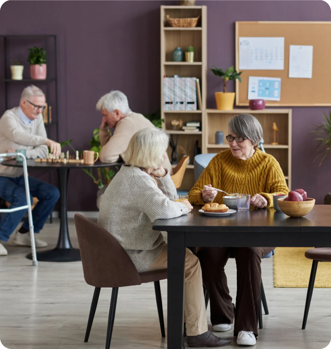 Seniors enjoying chess and coffee in a cozy room.