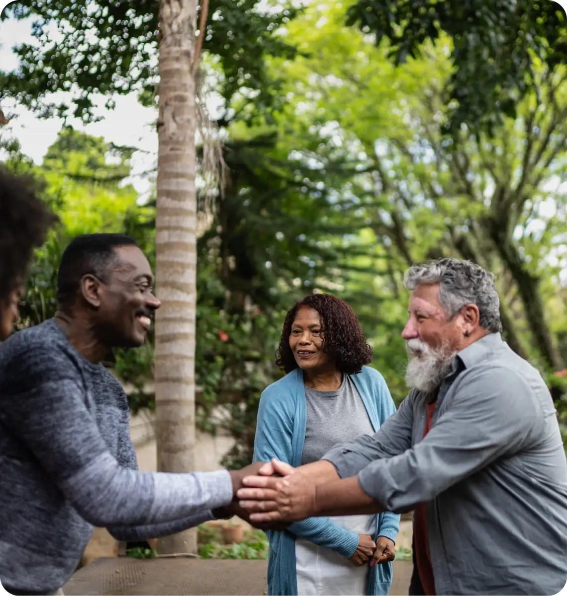 Two men shaking hands with a woman smiling in the background outdoors.