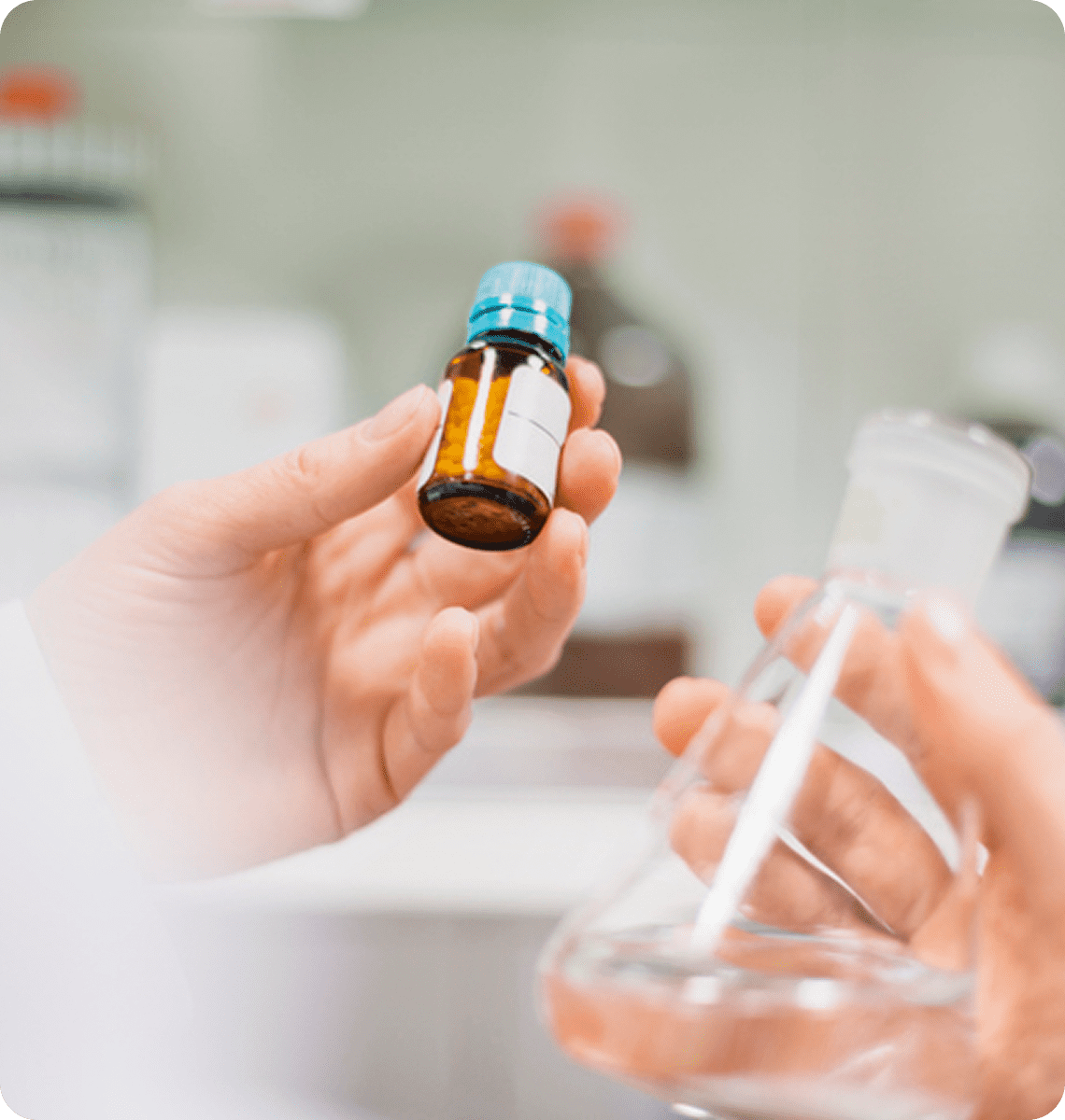 A hand holding a small medicine bottle with a dropper cap in a lab setting.
